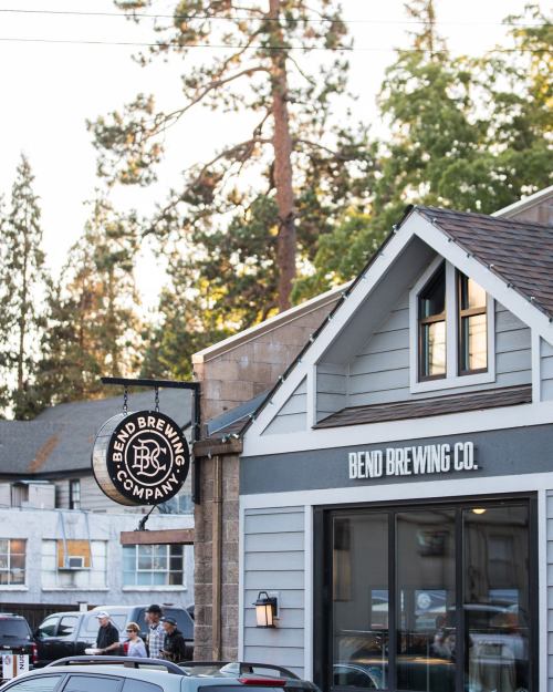 Sign for Bend Brewing Company on a building with trees in the background, showcasing a welcoming brewery atmosphere.