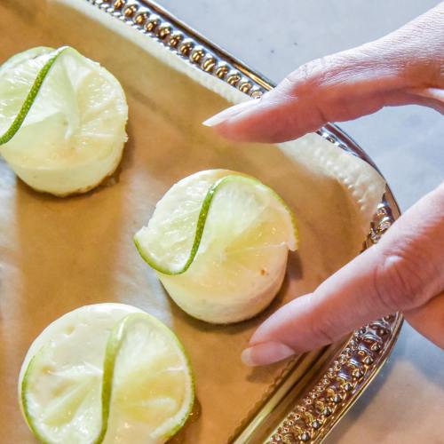 A hand reaching for small lime desserts on a decorative tray with lime slices on top.