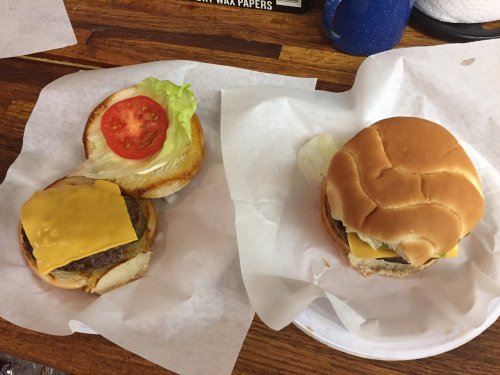 Two burgers on white paper: one with lettuce, tomato, and cheese, the other with just cheese on a plain bun.