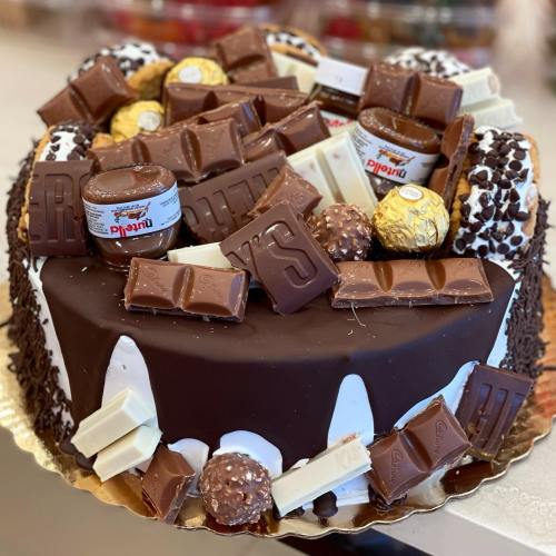 A decadent chocolate cake topped with various chocolates, including Nutella, Ferrero Rocher, and candy bars.
