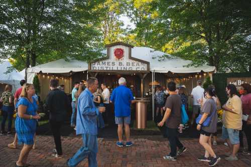 A crowd gathers outside a rustic food tent at an outdoor event, surrounded by trees and festive lighting.