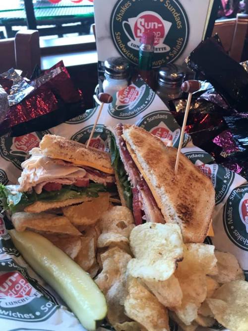 A delicious sandwich with lettuce, tomato, and turkey, served with chips and a pickle in a basket.