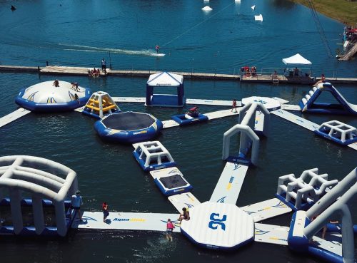 Aerial view of a water park with inflatable structures on a lake, featuring people enjoying various activities.