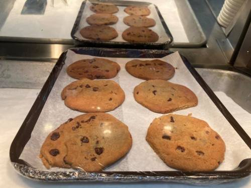 A tray of freshly baked chocolate chip cookies on parchment paper, with a shiny surface and a warm golden-brown color.