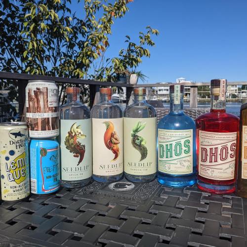A variety of spirits and non-alcoholic beverages displayed on a table outdoors, with a scenic background.