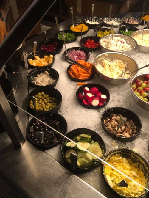 A variety of fresh toppings in bowls, including vegetables, fruits, and cheeses, arranged on a buffet table.