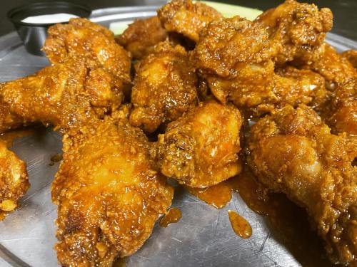 A platter of crispy, sauced chicken wings, glistening with a rich coating, served with a side of dipping sauce.