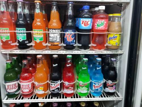A refrigerator filled with various colorful soda bottles, including brands like Jones, RC, and Frostie.