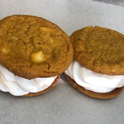 Two cookie sandwiches filled with fluffy white cream, resting on a sheet of parchment paper.