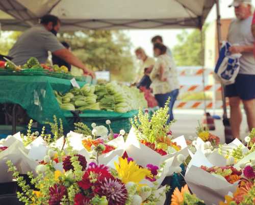 A vibrant farmers market scene with colorful flower arrangements and fresh produce on display under a tent.