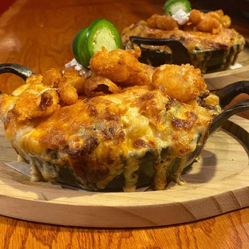 Two cheesy, baked dishes topped with crispy shrimp and jalapeño slices, served on wooden platters.