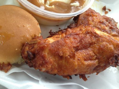 A crispy fried chicken wing, a soft roll, and a small cup of gravy on a white plate.