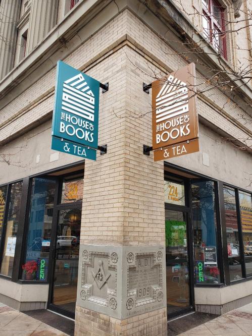 Signage for "The House of Books & Tea" on a corner building, featuring colorful signs and large windows.