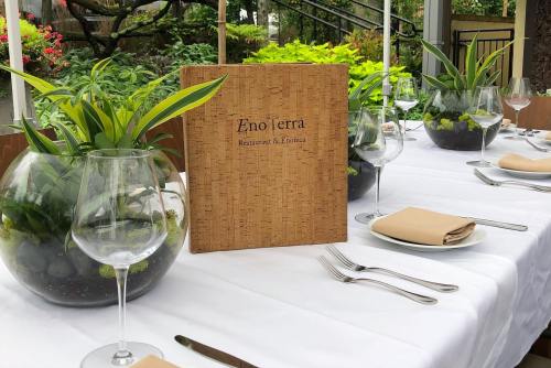 A beautifully set dining table with a menu, glassware, and potted plants in a serene outdoor setting.