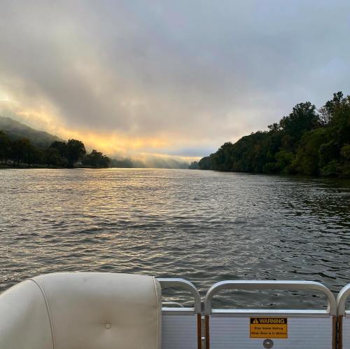 A serene river scene at dawn, with mist rising and trees lining the banks under a cloudy sky.