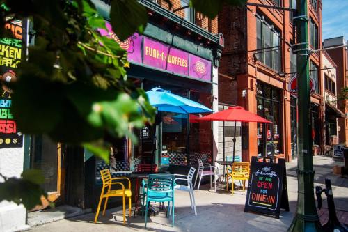 A colorful café with outdoor seating, featuring red and blue umbrellas, inviting diners to enjoy their meals.