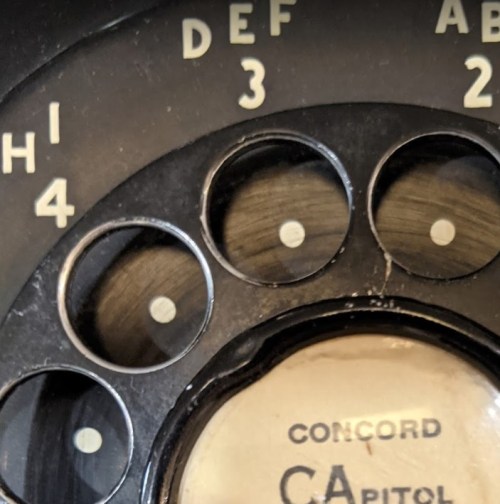 Close-up of a vintage rotary phone dial with numbers and letters, featuring "CONCORD" and "CAPITOL."