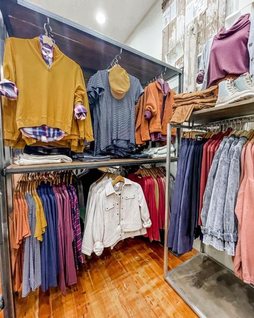 A clothing display featuring various tops in warm colors, neatly arranged on hangers and shelves.