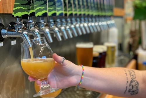 A hand pours a hazy beer into a glass from a row of taps at a brewery.