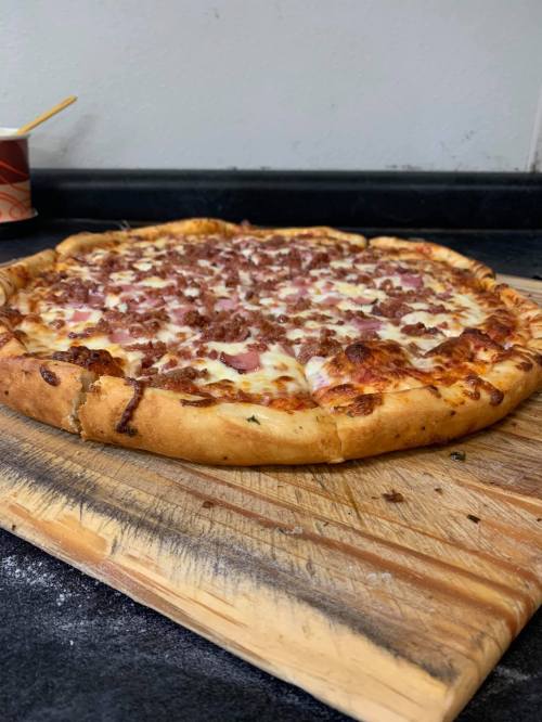 A freshly baked pizza with a golden crust, topped with cheese and chunks of meat, resting on a wooden cutting board.
