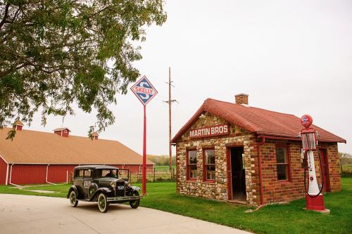 A vintage car parked near a historic stone building with a "Martin Bros" sign and a retro gas pump.