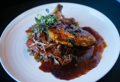 A plated dish featuring roasted chicken with a glossy sauce, served on a bed of grains and garnished with microgreens.