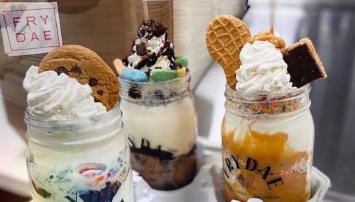 Three colorful ice cream sundaes in jars, topped with whipped cream, cookies, and various candies.