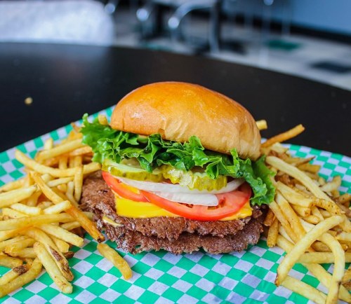 A juicy burger with lettuce, tomato, pickles, and cheese, served with a side of crispy French fries on a green checkered plate.