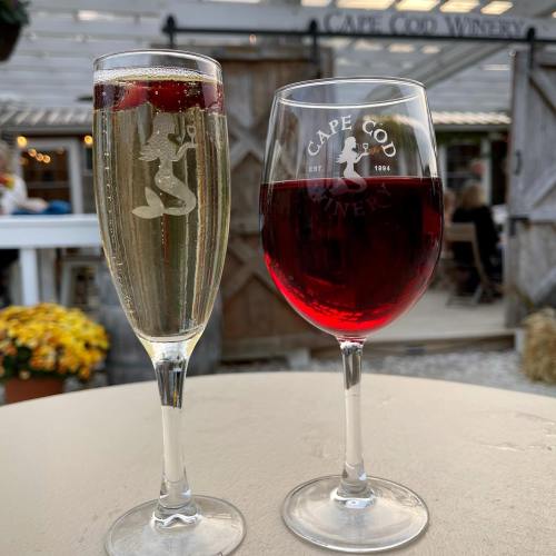 Two glasses of wine: one filled with sparkling wine and cherries, the other with red wine, set against a winery backdrop.