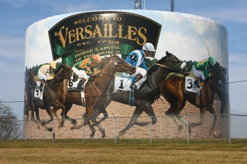 Mural on a water tower depicting horse racing, with jockeys in colorful silks and the text "Welcome to Versailles."