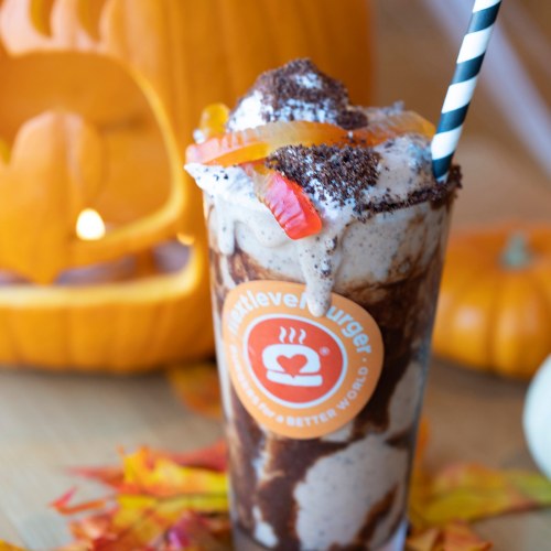 A festive milkshake topped with candy and chocolate, with a pumpkin decoration in the background.