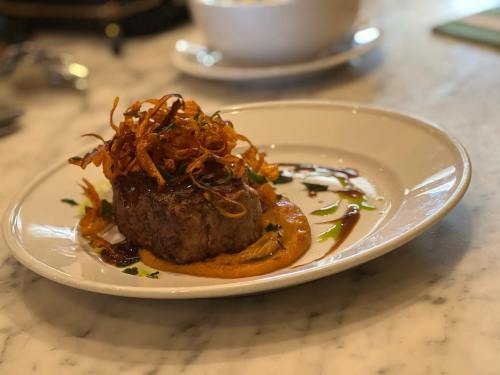 A gourmet dish featuring a beef patty topped with crispy onions on a bed of orange puree, garnished with herbs.