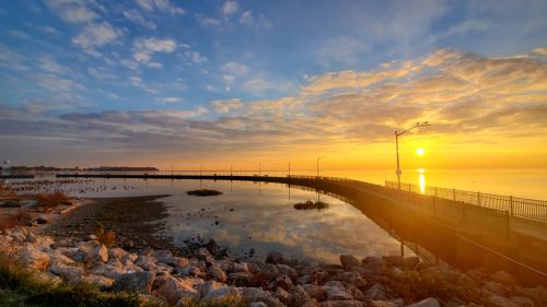 Sunrise over a calm lake, with a pier extending into the water and clouds reflecting warm colors in the sky.