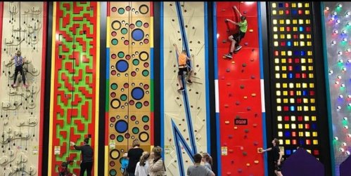 A colorful indoor climbing gym with various climbing walls and people climbing different routes.