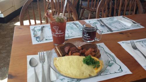 A breakfast plate featuring an omelet, bacon, potatoes, and toast, alongside a Bloody Mary and coffee on a wooden table.