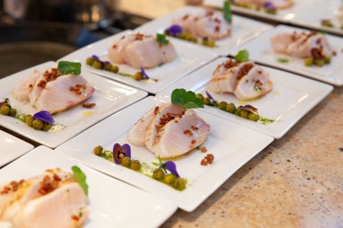 Plates of elegantly arranged fish fillets garnished with herbs, nuts, and edible flowers on a countertop.