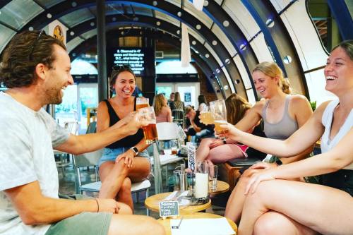 A group of four friends joyfully toasting with drinks in a lively bar setting.