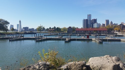 A serene waterfront view featuring docks, a lighthouse, and a city skyline under a clear blue sky.