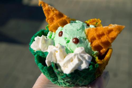 A colorful ice cream dessert in a waffle bowl, featuring mint green ice cream, whipped cream, and cone "ears."
