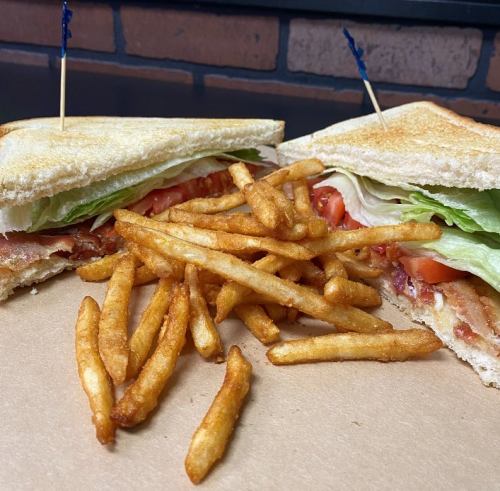 A sandwich with bacon, lettuce, and tomato, served with a side of golden French fries on a brown paper surface.