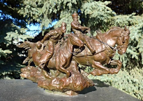 A bronze sculpture of two riders on horseback, captured in motion, surrounded by greenery.