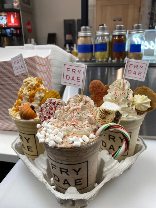 A tray of festive milkshakes topped with whipped cream, sprinkles, and decorative flags from Frydae.