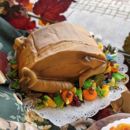 A cake shaped like a roasted turkey, decorated with colorful frosting leaves and autumn-themed accents.