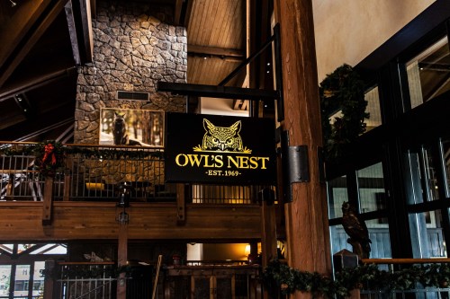 Sign for "Owl's Nest" established in 1969, displayed in a rustic wooden interior with stone accents.