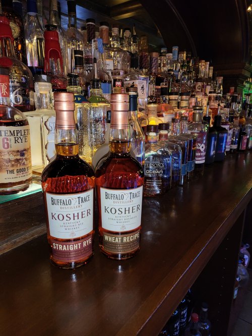 Two bottles of Buffalo Trace Kosher whiskey on a bar shelf, surrounded by various liquor bottles in the background.