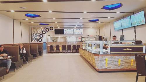 Interior of a modern restaurant with seating, a service counter, and digital menus displayed on the wall.