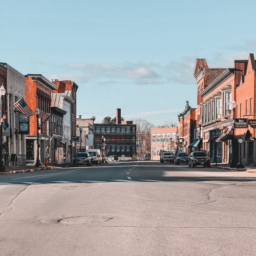 A quiet street lined with historic buildings and parked cars under a clear blue sky.