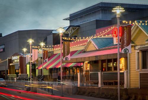 A vibrant street scene featuring colorful buildings, string lights, and banners in an urban setting at dusk.