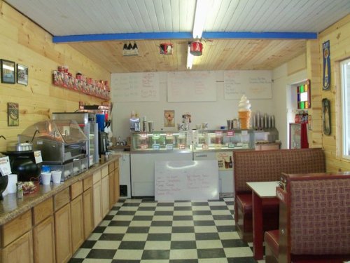 Cozy ice cream shop interior with wooden walls, checkered floor, and a service counter displaying various treats.