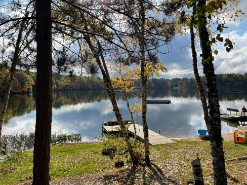 A serene lake view surrounded by trees, with a dock and colorful autumn foliage reflecting on the water.